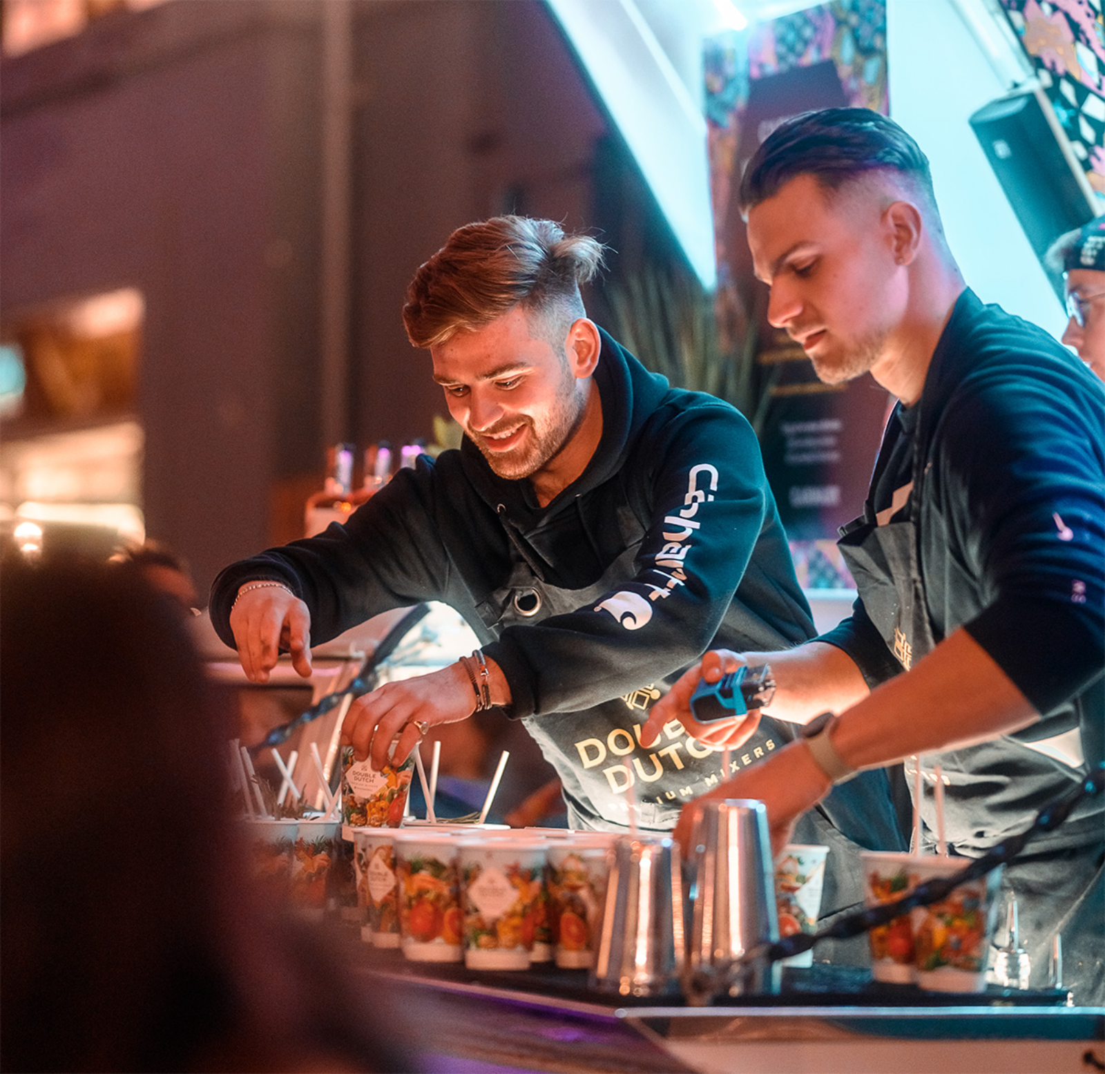 Two Beetle Juice bartenders mixing cocktails behind a busy branded bar at an event